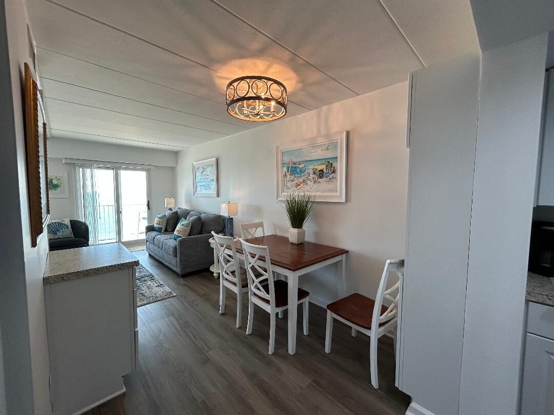 A modern kitchen with white cabinetry, a dining area with a wooden table and white chairs, and a hanging light fixture.