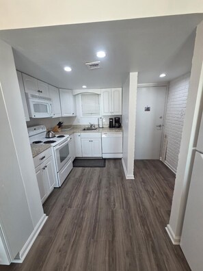 Una cocina compacta con gabinetes blancos, microondas, estufa y cafetera.