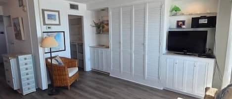 Ein Zimmer mit Holzboden, einem Fernseher, einem Sofa und einem Essbereich mit Tisch und Stühlen.