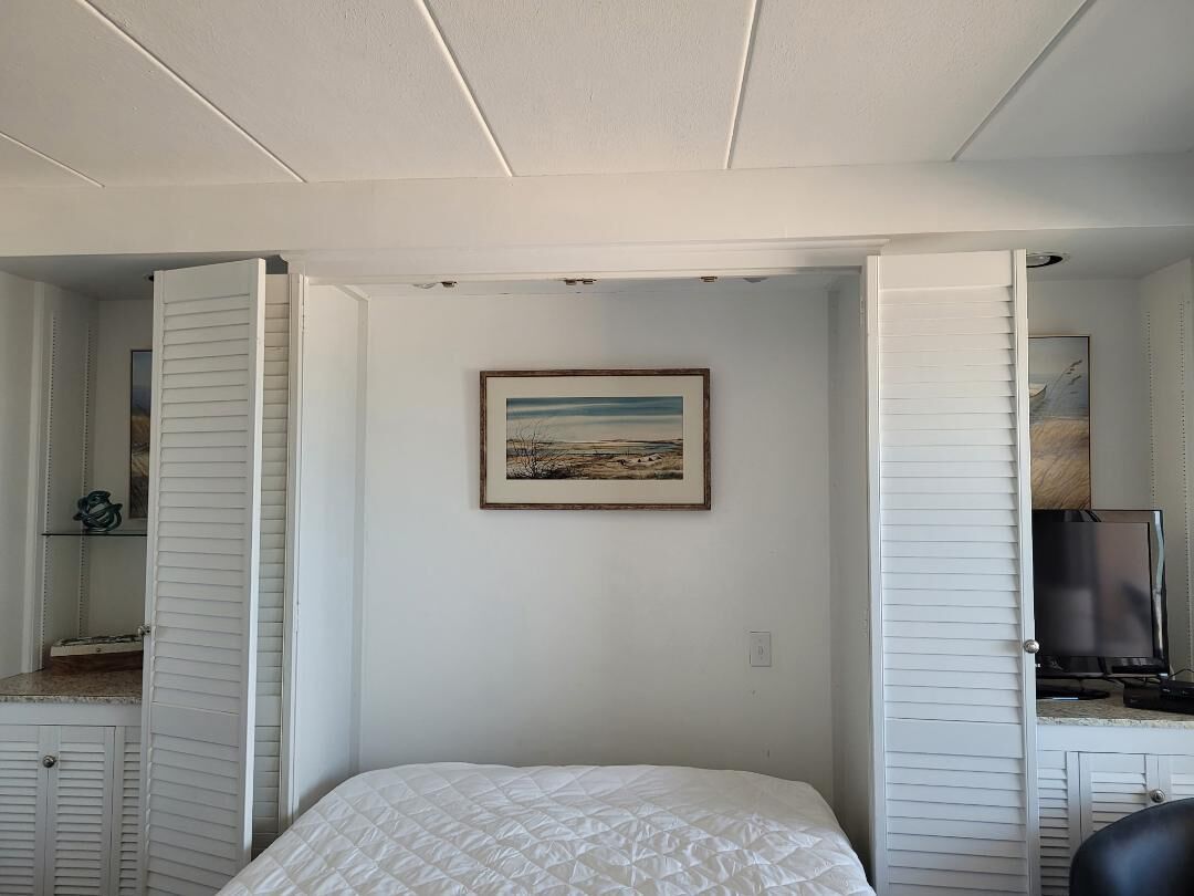 A bedroom with a bed, a painting on the wall, and a television on a stand.