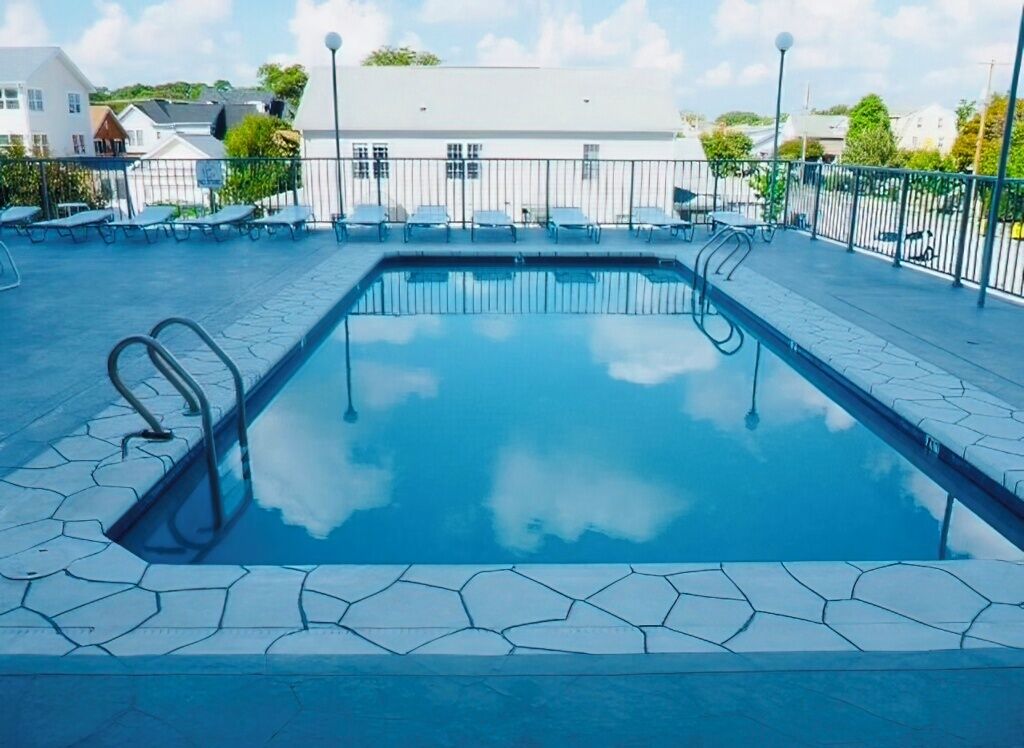 A rectangular swimming pool with a clear blue water surface, surrounded by a tiled deck and metal railings.