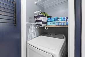 Un espace buanderie comprenant un lave-linge, un étendoir et des serviettes pliées.