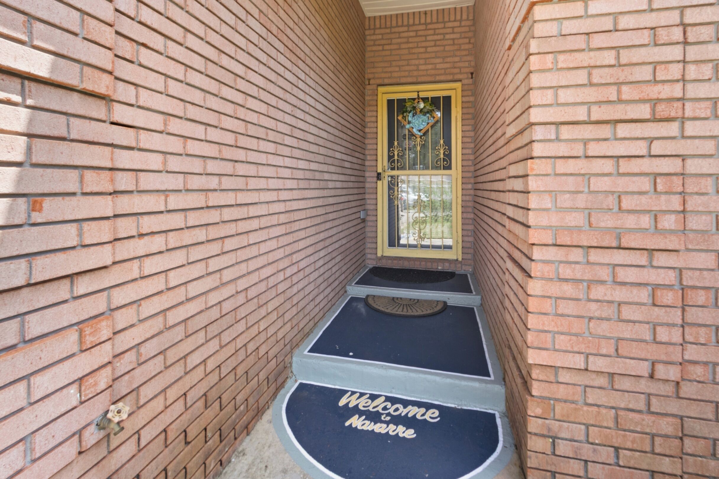 A narrow brick corridor with a door featuring a decorative glass panel and a welcome mat.