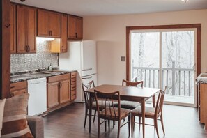 Une cuisine avec des meubles en bois, un réfrigérateur blanc, une table à manger avec des chaises et une grande porte-fenêtre coulissante donnant sur un balcon.