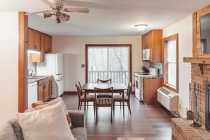A spacious kitchen with wooden cabinets, a dining table with chairs, a ceiling fan, and a large window with a view of trees. - Gorgeous Views • Hot Tub Getaway • Secluded Cabin (Logan)