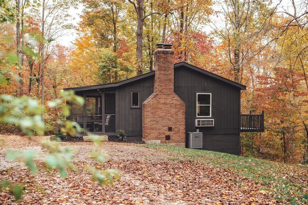 A cabin with a brick chimney, surrounded by autumn foliage.