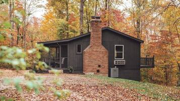 A cabin with a brick chimney, surrounded by autumn foliage.