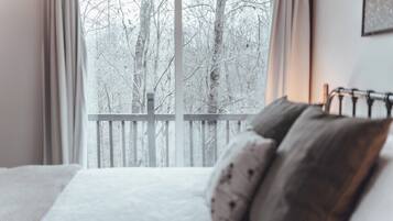 Ein Schlafzimmer mit einem Bett, Kissen und Blick auf einen verschneiten Wald durch ein Fenster.