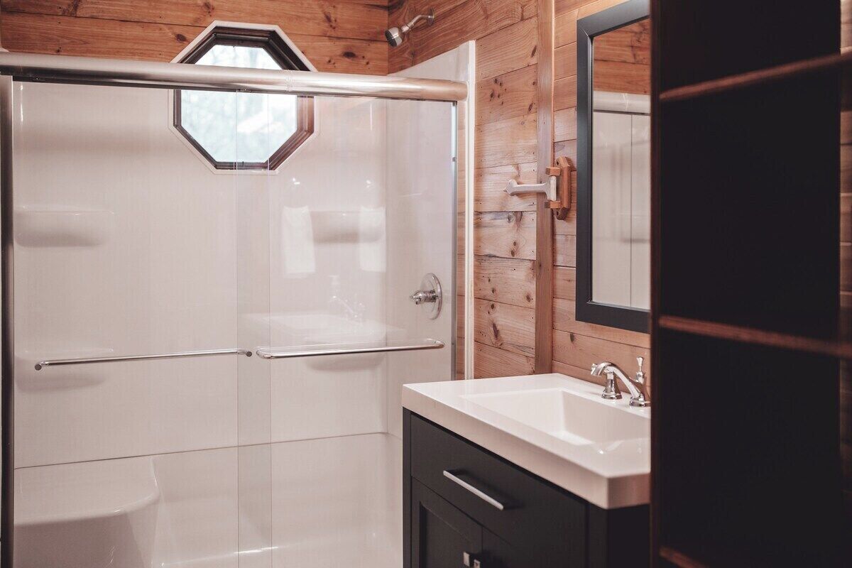 Een moderne badkamer met een douchecabine van glas, een wit wastafelmeubel en houten lambrisering.