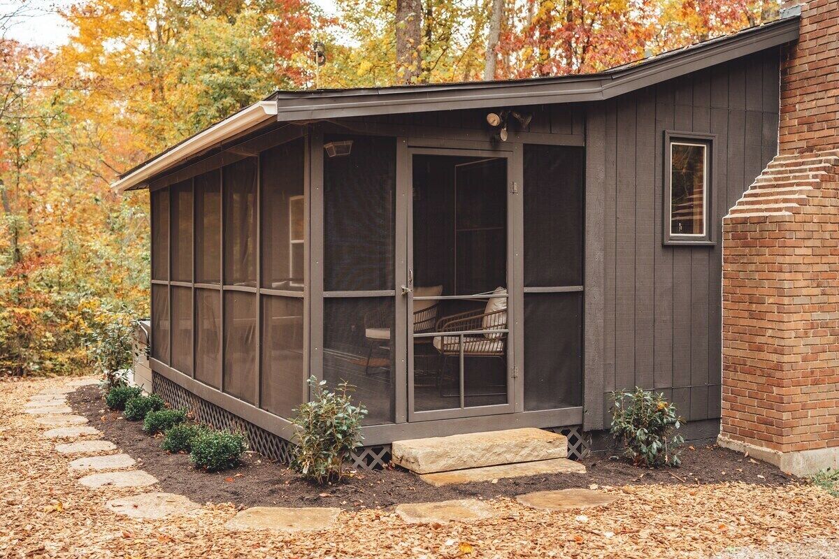 A covered outdoor seating area with a bench, a small table, and a window.