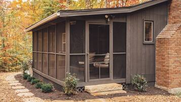 A covered outdoor seating area with a bench, a small table, and a window.