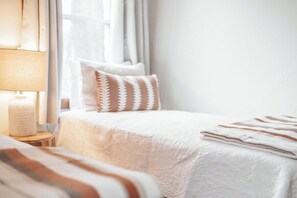 A neatly made bed with a striped blanket, a bedside lamp, and a window with curtains. - Gorgeous Views • Hot Tub Getaway • Secluded Cabin (Logan)