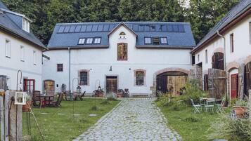 A courtyard with a cobblestone path leading to a building with a gabled roof and multiple windows.