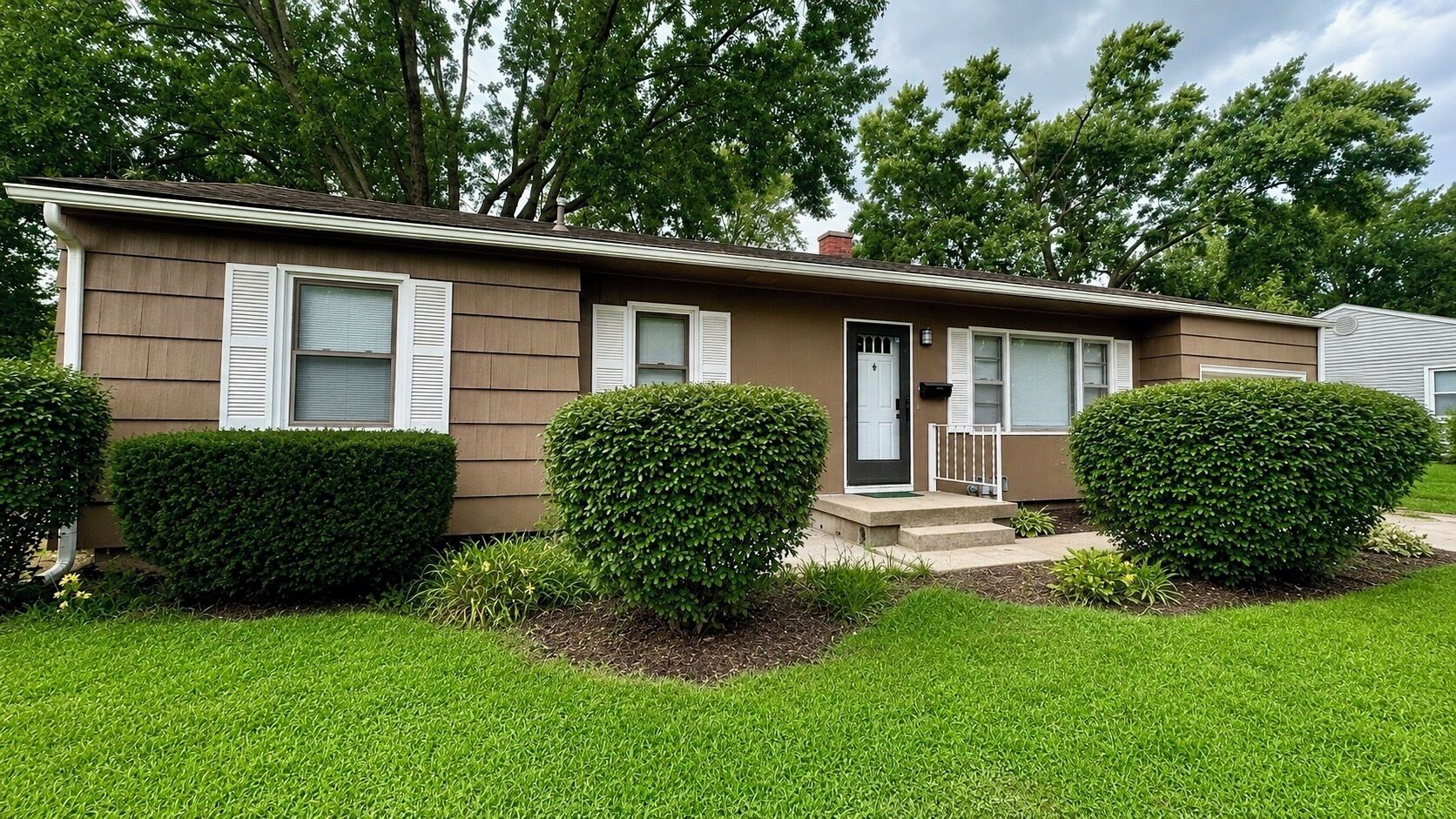 A single-story house with a front porch, a door, and two windows with shutters.