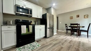 A modern kitchen with white cabinets, a stainless steel refrigerator, and a dining area with wooden chairs and a table.