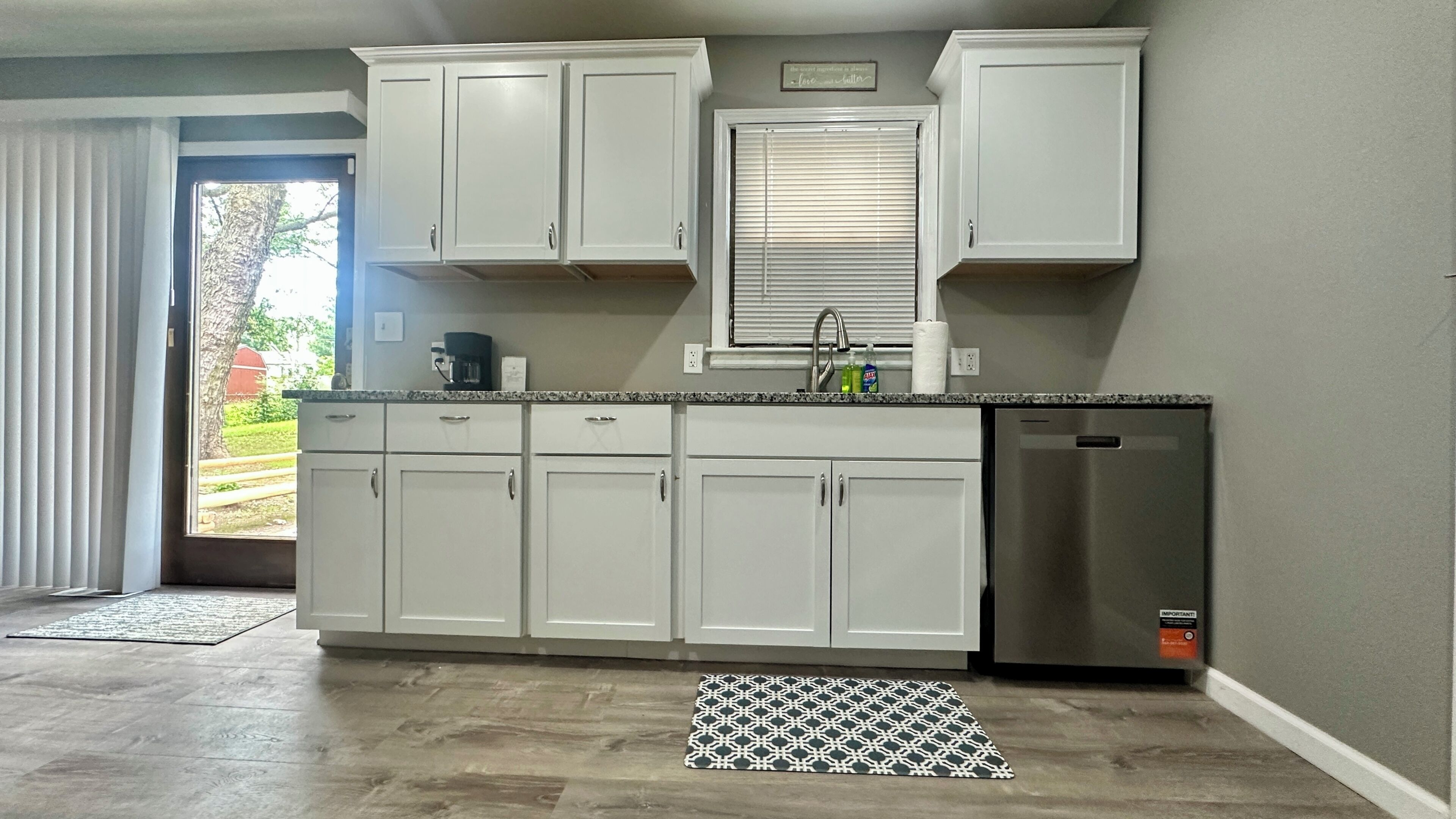 A kitchen with white cabinets, a stainless steel refrigerator, and a window with blinds.
