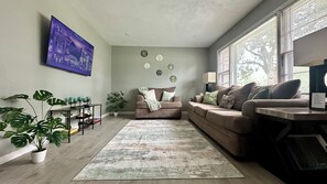 Una sala de estar con sofá, mesa de centro y televisión de pantalla plana montada en la pared.