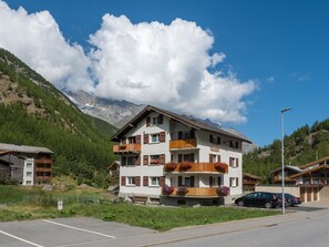 Ein mehrstöckiges Hotel mit Balkonen, einem Parkplatz und einer Bergkulisse im Hintergrund.