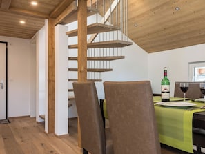 Ein modernes Interieur mit einer Holztreppe, einem Essbereich mit Tisch für zwei Personen und einer Weinflasche.