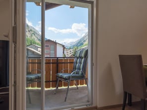 Ein Zimmer mit einer Schiebetür zu einem Balkon mit Blick auf Berge und Häuser.