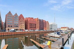 A waterfront marina with docked boats, a clear sky, and buildings with distinct architectural styles. - Granaria B104 | TOP Location (Gdańsk)