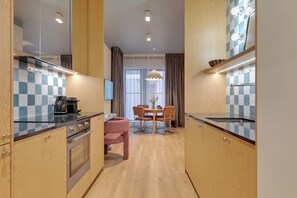 A modern kitchen with wooden cabinets, a dining area with a table and chairs, and a large window with curtains. - Granaria B104 | TOP Location (Gdańsk)