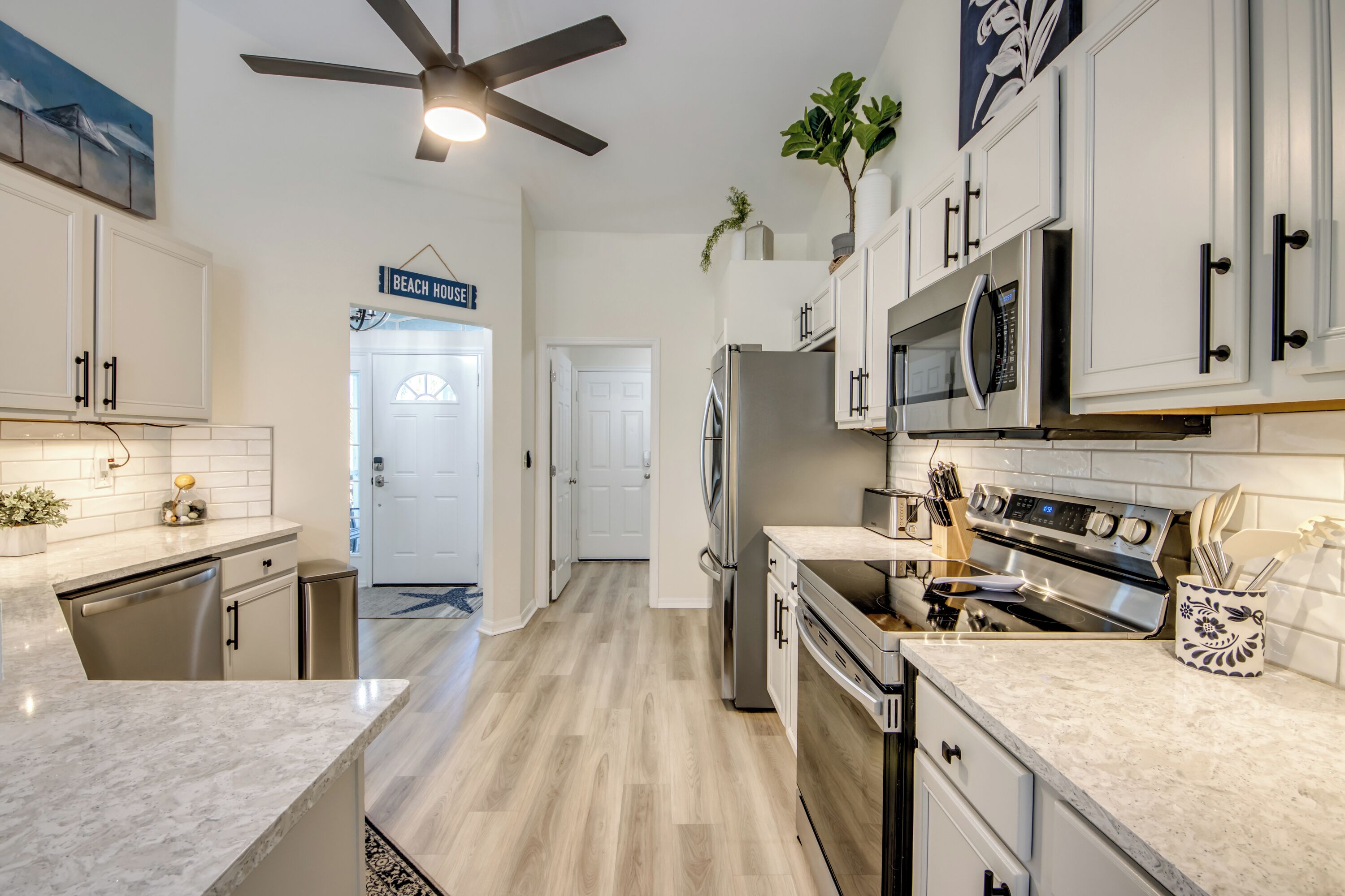 A modern kitchen with white cabinets, stainless steel appliances, and a ceiling fan.