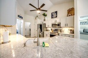 A modern kitchen with a central island, stainless steel appliances, and a ceiling fan. - Blue Heaven Rendezvous — 4 BR/ 2 bath retreat in SW Cape Coral with  heated pool and spa, bicycles, and fully fenced backyard (Cape Coral)