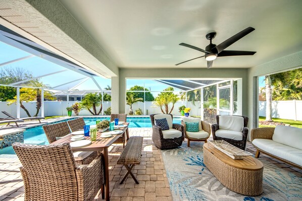 Eine überdachte Terrasse im Freien mit Pool, Korbmöbeln und Deckenventilator.