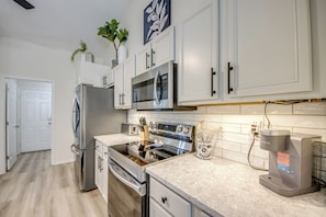 A modern kitchen with stainless steel appliances, white cabinetry, and a marble countertop. - Blue Heaven Rendezvous — 4 BR/ 2 bath retreat in SW Cape Coral with  heated pool and spa, bicycles, and fully fenced backyard (Cape Coral)