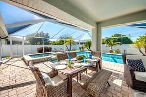 A covered patio with a pool, wicker furniture, and a table set for dining. - Blue Heaven Rendezvous — 4 BR/ 2 bath retreat in SW Cape Coral with  heated pool and spa, bicycles, and fully fenced backyard (Cape Coral)