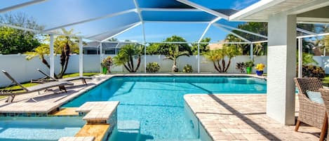 A clear blue swimming pool with a sunshade structure, surrounded by a white fence and various plants.