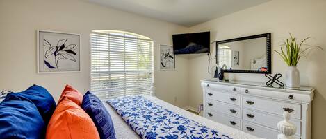 A bedroom with a bed, a dresser, a television, and artwork on the walls.
