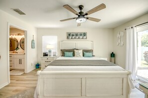 A bedroom with a bed, a ceiling fan, a window with blinds, a bedside table, and a nightstand. - Blue Heaven Rendezvous — 4 BR/ 2 bath retreat in SW Cape Coral with  heated pool and spa, bicycles, and fully fenced backyard (Cape Coral)