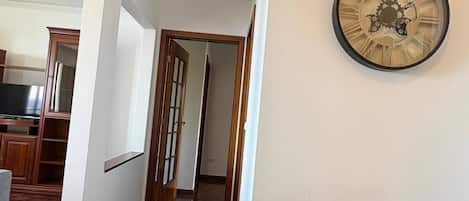 Un couloir doté d’un plancher en bois, d’une horloge au mur et d’une petite table en bois.