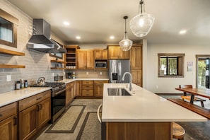 A modern kitchen with wooden cabinets, stainless steel appliances, and a large island with a sink. - Paradise Condo 100,Hot Tub,Mtn.Views, Lift .5 Mile (Sandpoint)