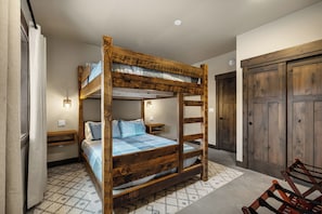 A bunk bed with a wooden frame and a mattress with a blue and white checkered blanket. There is a small bedside table with a lamp, a wall-mounted light, and a door with a wooden frame. - Paradise Condo 100,Hot Tub,Mtn.Views, Lift .5 Mile (Sandpoint)