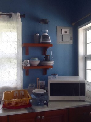 Une cuisine équipée d’un four à micro-ondes, d’étagères remplies de vaisselle, d’un mixeur et d’une fenêtre.