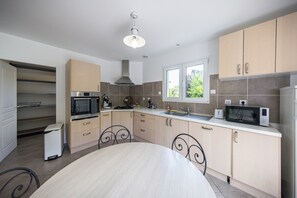 A compact kitchen with a dining table, built-in oven, microwave, and a window providing natural light. - Large House for 12 People with 2 Vacation Rentals - 220 m² - 10 Beds (Meurthe-et-Moselle)