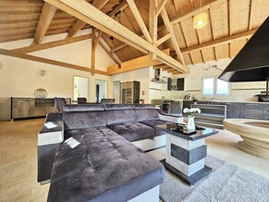 A spacious living room with a large sectional sofa, a kitchen in the background, and a high ceiling with exposed wooden beams. - Large House for 12 People with 2 Vacation Rentals - 220 m² - 10 Beds (Meurthe-et-Moselle)