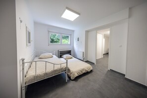 A bedroom with two beds, a window, a radiator, and a door leading to another room. - Large House for 12 People with 2 Vacation Rentals - 220 m² - 10 Beds (Meurthe-et-Moselle)