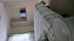 Um quarto com uma cama, uma janela pequena e uma televisão presa à parede.