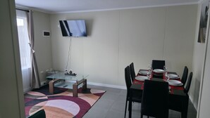 A dining area with a glass table, black chairs, and a flat-screen TV mounted on the wall. - A Peaceful Retreat in Bosquemar (Los Lagos)