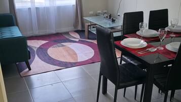 A dining area with a glass table, black chairs, a red placemat, and a television mounted on the wall.