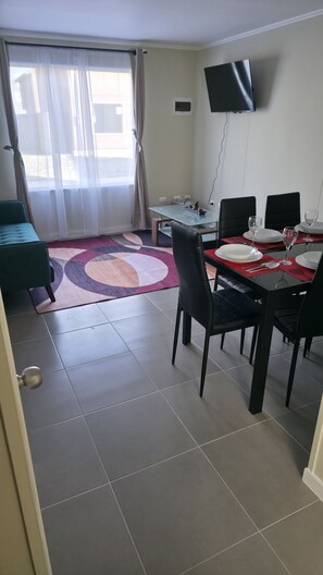 A dining area with a glass table, black chairs, a red placemat, and a television mounted on the wall.