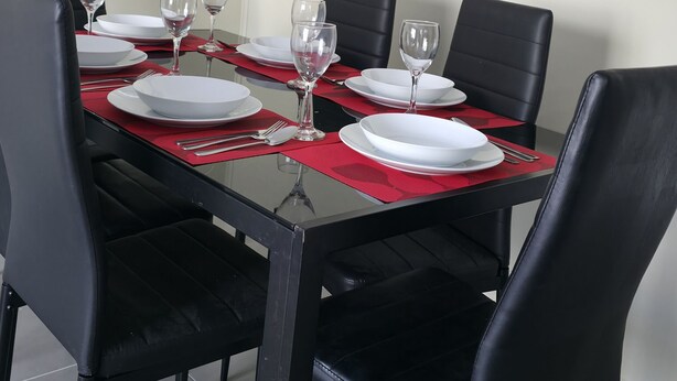 A dining area with a glass table, black chairs, and a painting on the wall. - A Peaceful Retreat in Bosquemar (Los Lagos)