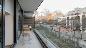 Ein Balkon mit Holztisch und -stühlen, einem Blumentopf und Blick auf die Straße mit Gebäuden und Bäumen.