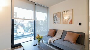 Ein modernes Wohnzimmer mit einem grauen Sofa, einem Couchtisch und einem großen Fenster mit Blick auf die Straße.