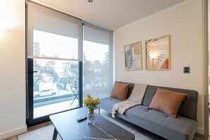 Ein modernes Wohnzimmer mit einem grauen Sofa, einem Couchtisch und einem großen Fenster mit Blick auf die Straße.