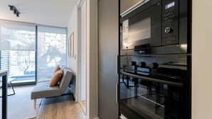 A modern kitchen with a built-in oven and microwave, a dining area with a sofa and table, and a large window offering a view of the outside.
